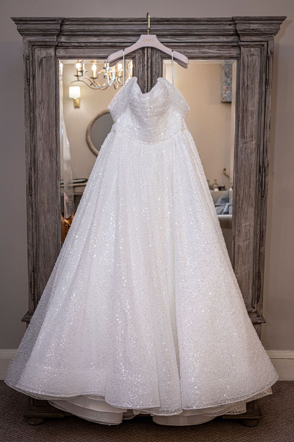 Sparkling white wedding dress with full skirt displayed on rustic wooden hanger.