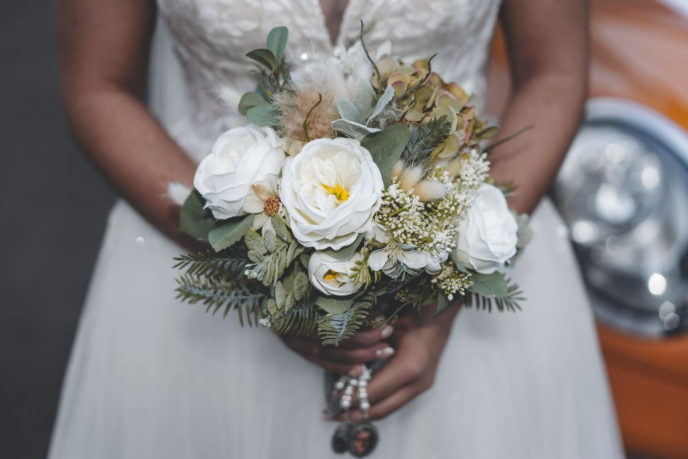Elegant white bridal bouquet with roses and greenery held against a wedding dress.