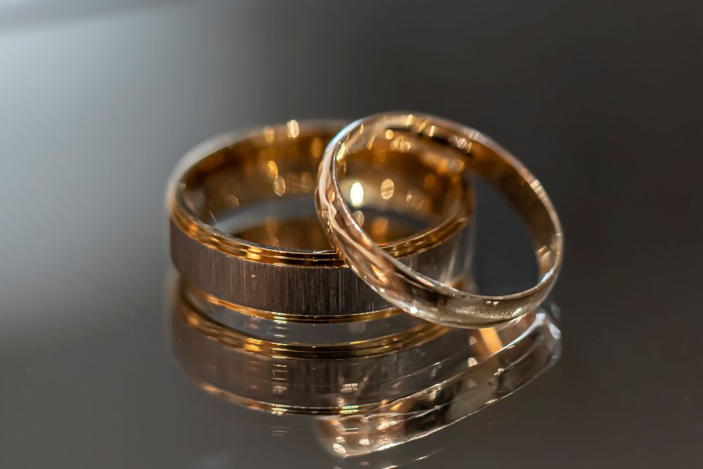 Gold wedding bands with textured details reflecting on dark glossy surface.