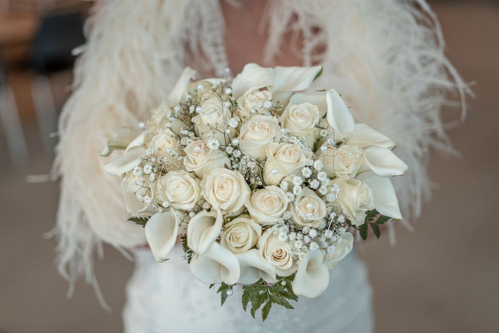 Elegant white rose bridal bouquet with feather accents.
