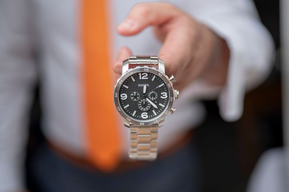 Close-up details of a silver wristwatch being adjusted against a dark background.