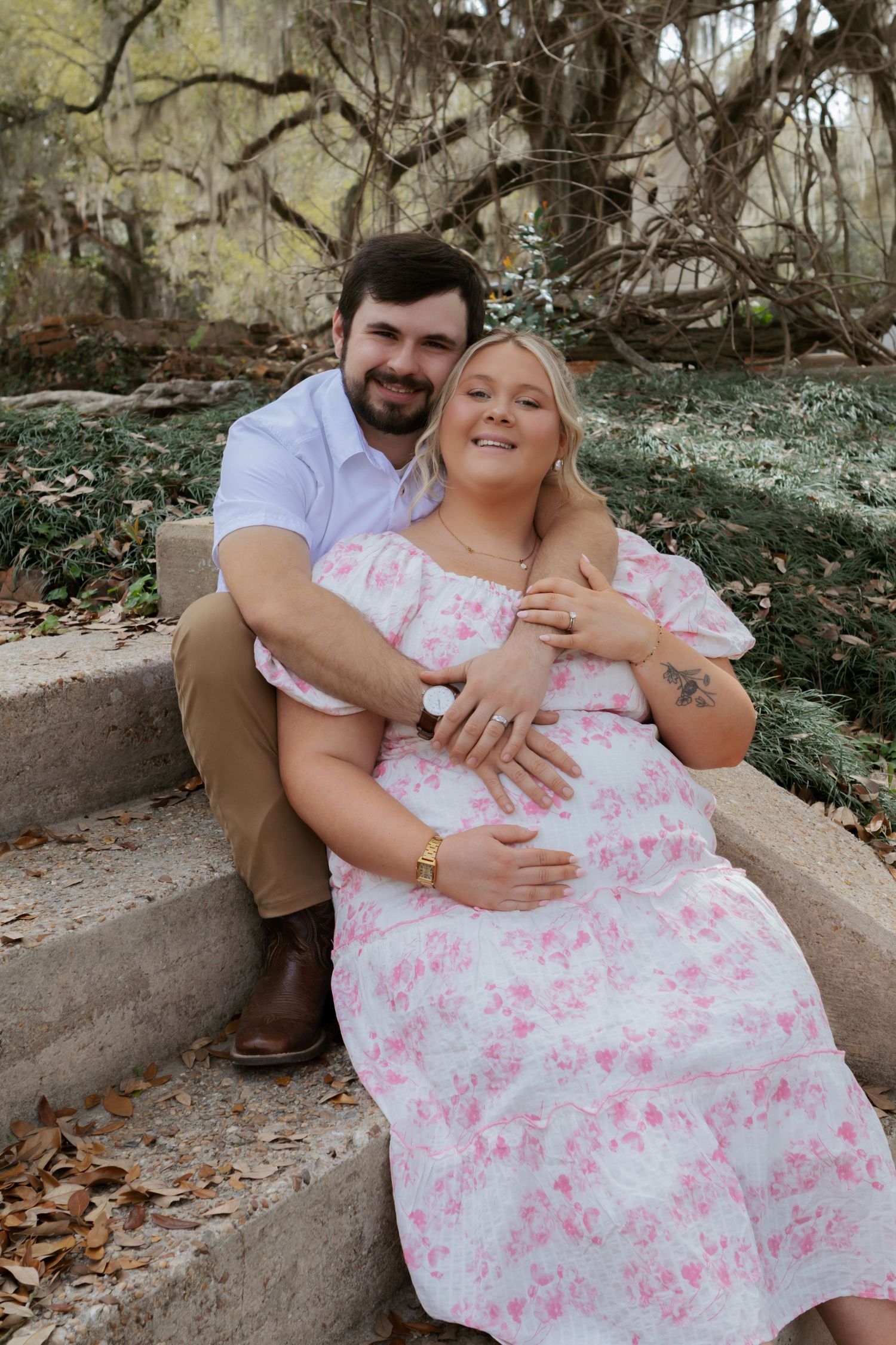 A couple sits together on stone steps outdoors while sharing a tender embrace in a romantic photoshoot setting.
