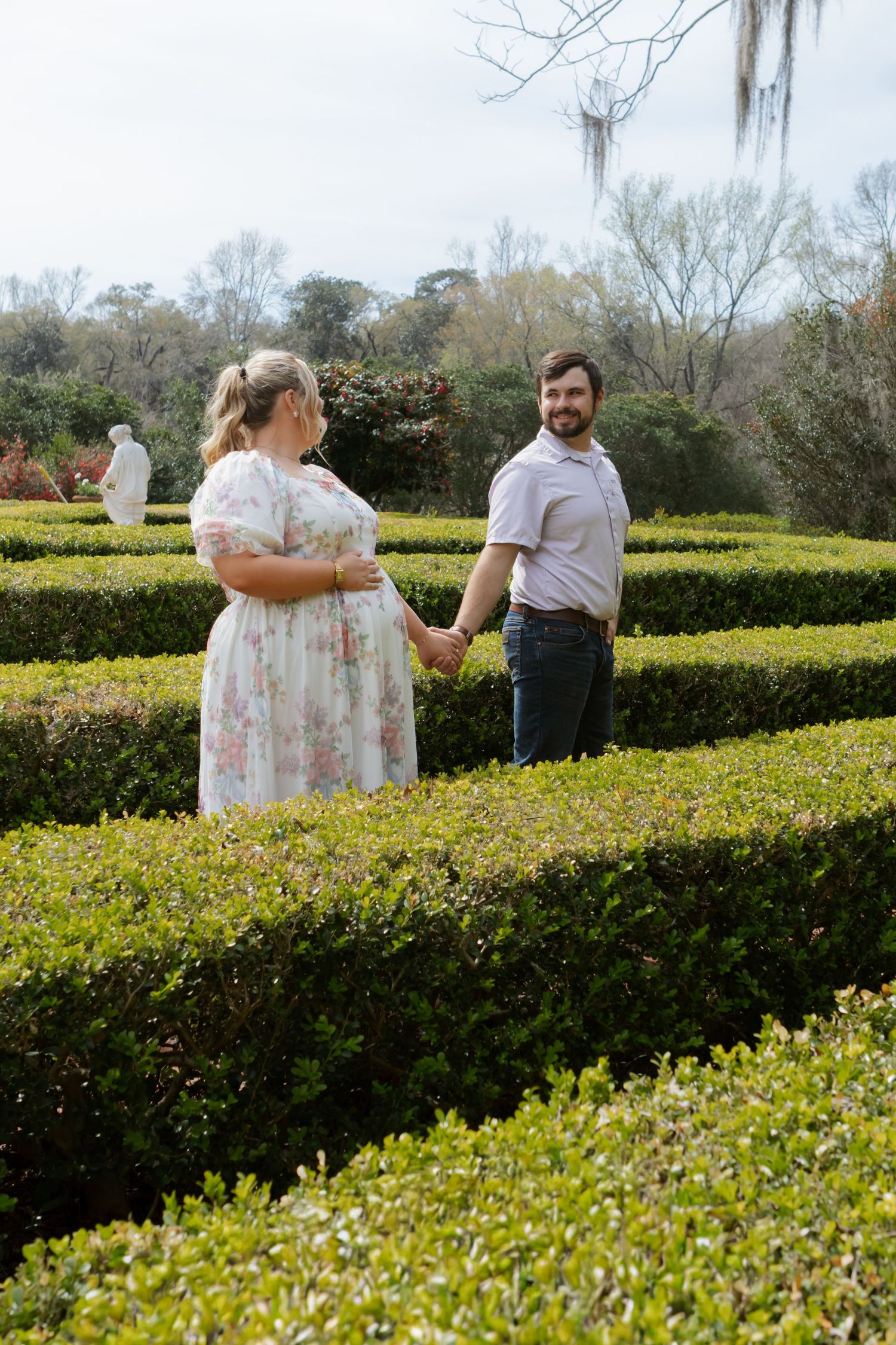 A couple stands together in a formal garden with manicured hedges and springtime greenery at a historic estate.
