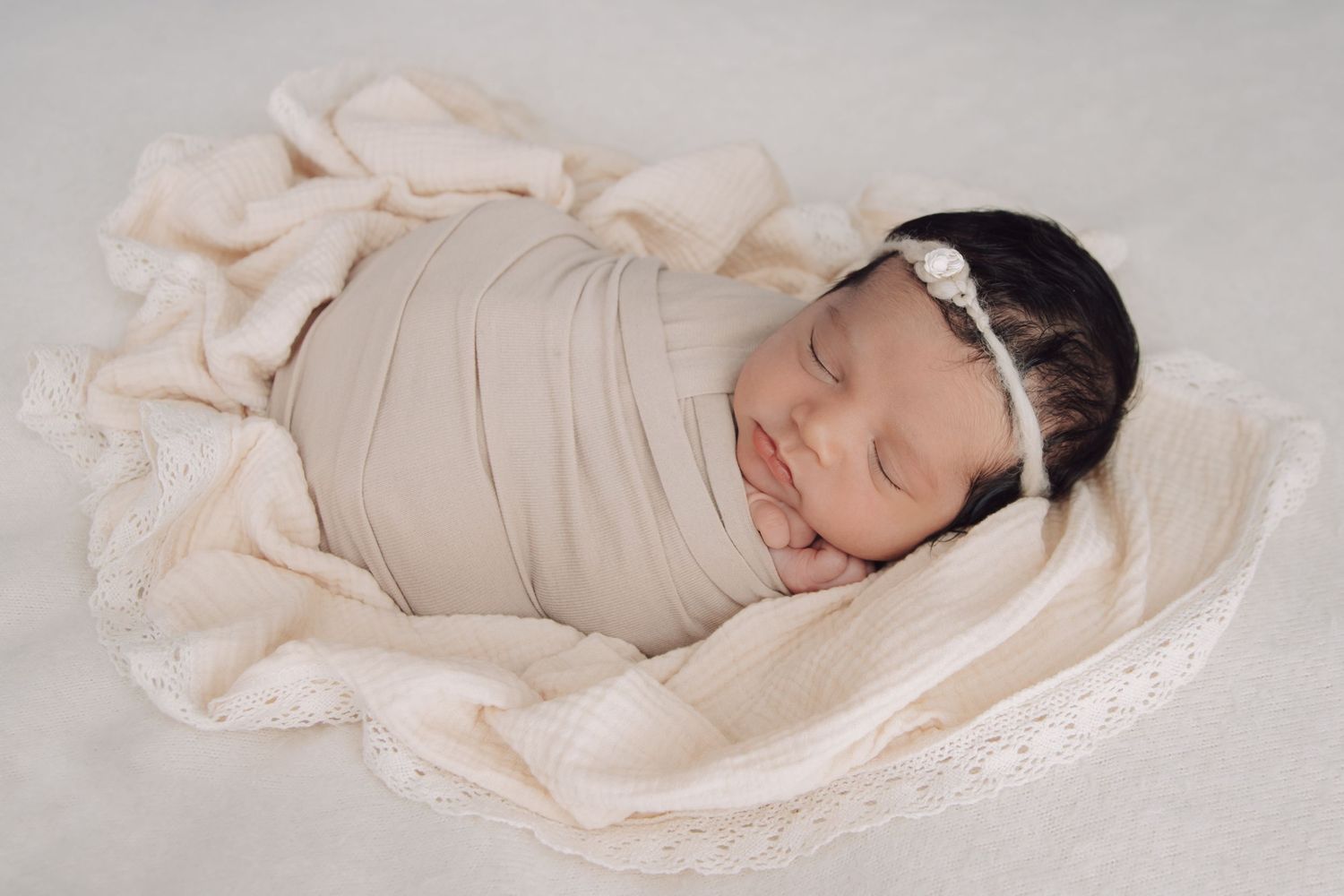 A sleeping newborn in black and white wearing a delicate floral crown and wrapped in a pearl-adorned blanket.