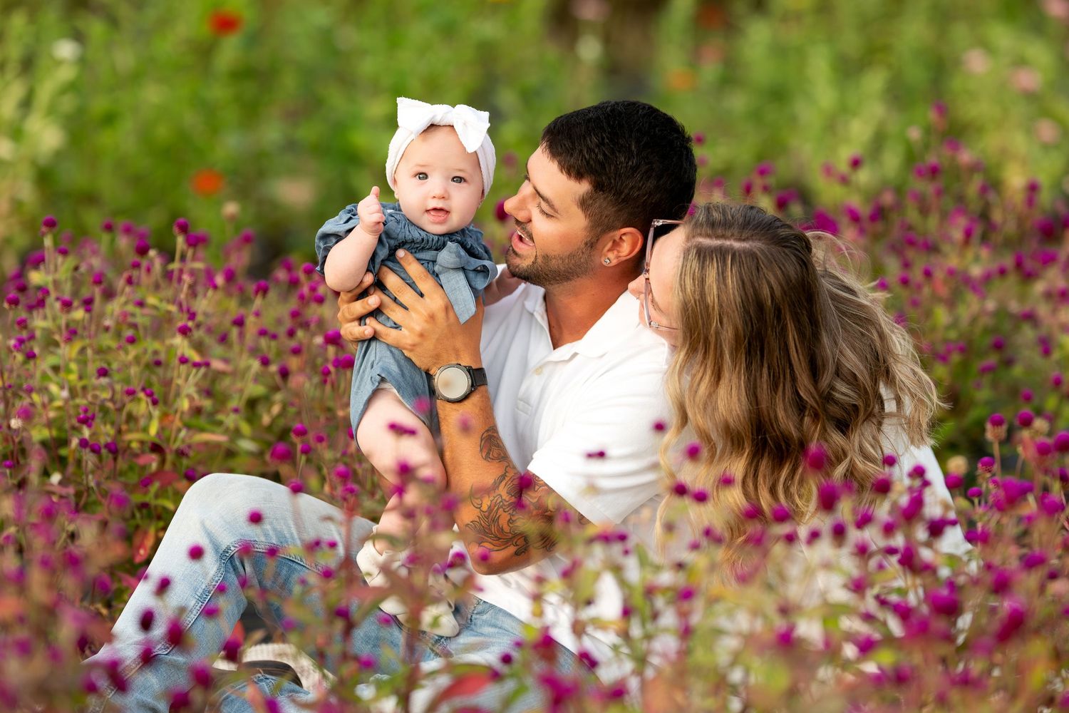 Happy family with baby sitting together in a vibrant purple flower field outdoors.