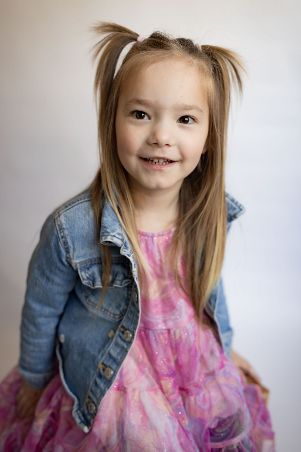 Cute smiling little girl with pigtails wearing pink dress and denim jacket.