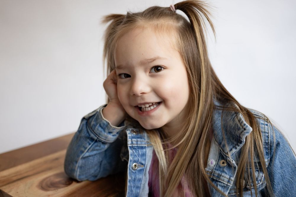 Adorable smiling little girl with pigtails in denim jacket resting head on hand.