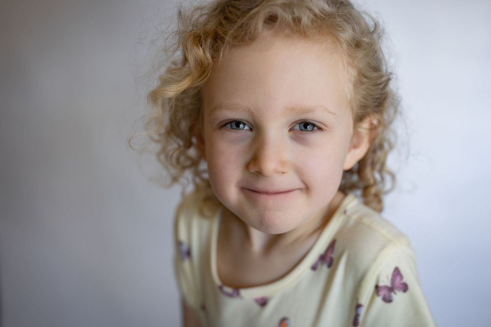 A close-up portrait of a curly-haired young girl smiling softly at the camera.