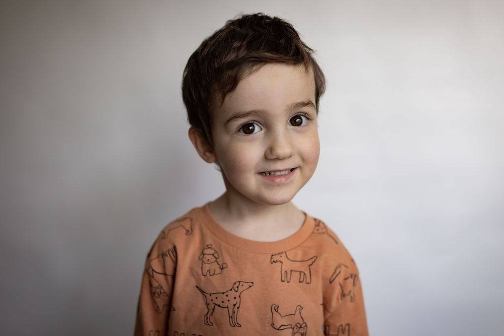A young boy in an orange dog-print long-sleeve shirt smiles gently for his portrait.