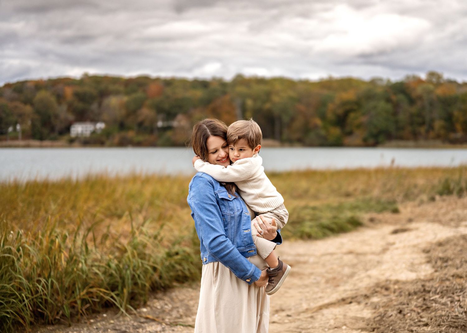 A couple shares tender moments along a scenic autumn path near a lake surrounded by fall foliage.