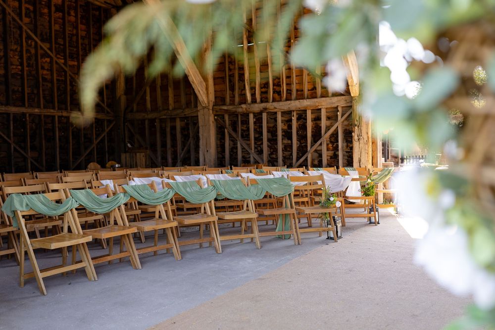 Sunlit wooden barn interior set up for a wedding ceremony with rows of benches and natural light streaming in.