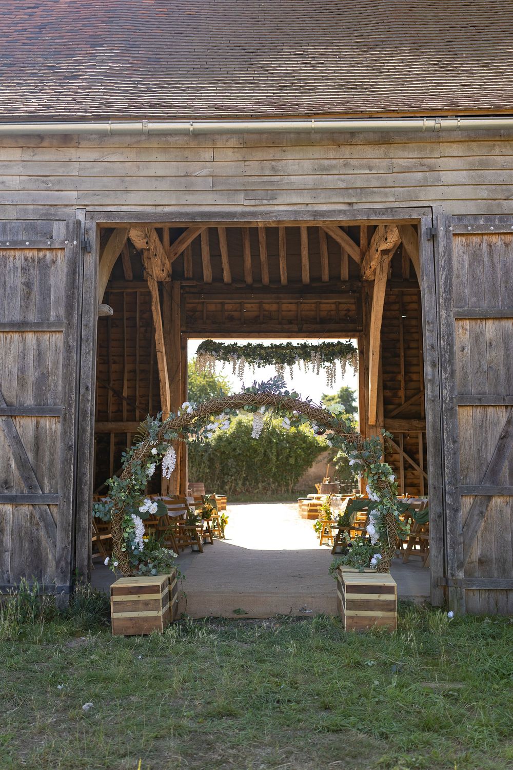 Rustic wooden barn exterior with multiple open doors decorated with floral arrangements.