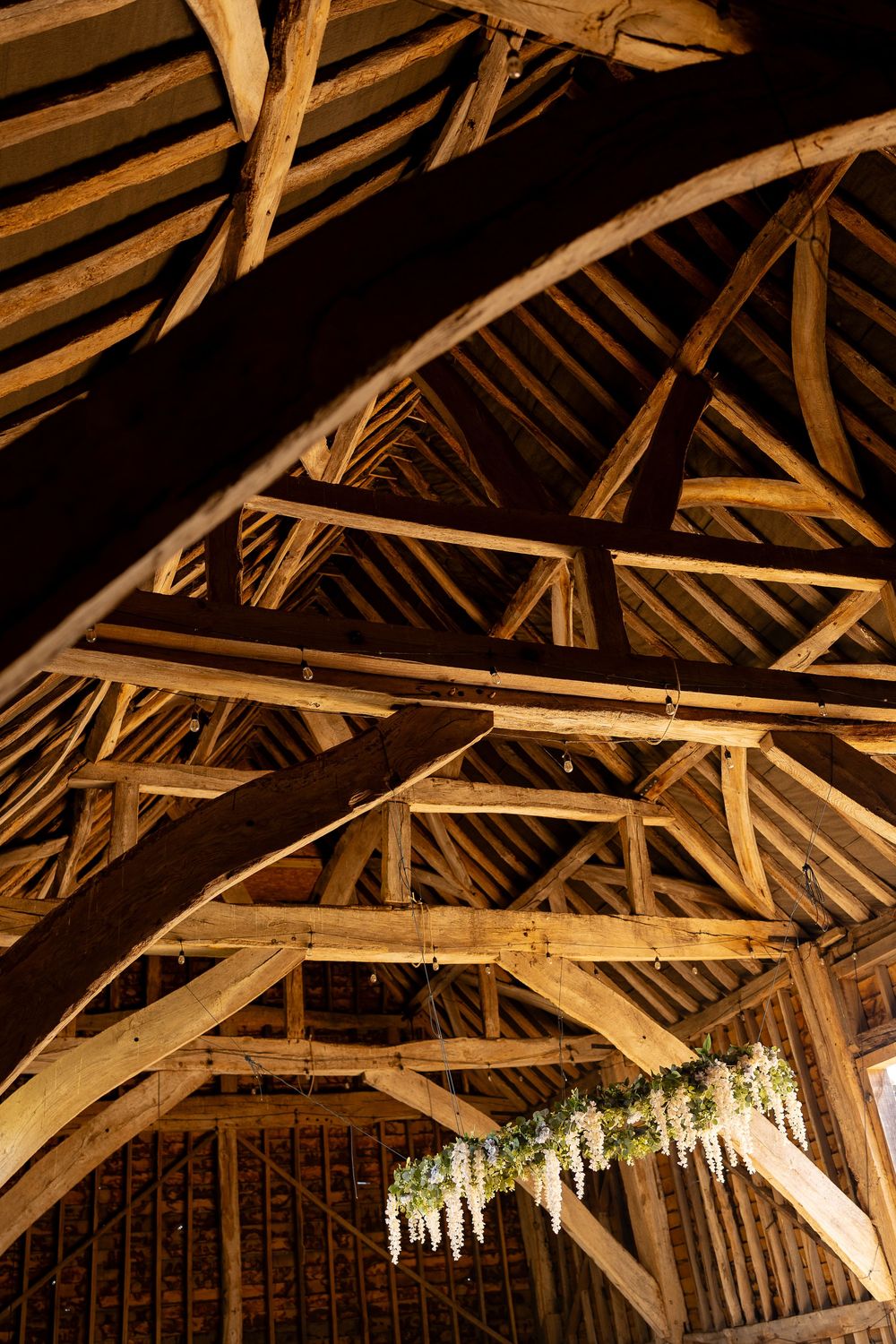 Rustic wooden barn rafters decorated with hanging floral arrangements for wedding reception.