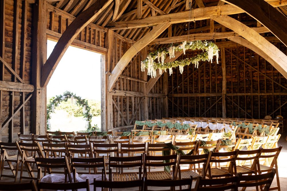 Rustic wooden barn interior set up for wedding ceremony with rows of chairs and exposed beam ceiling.