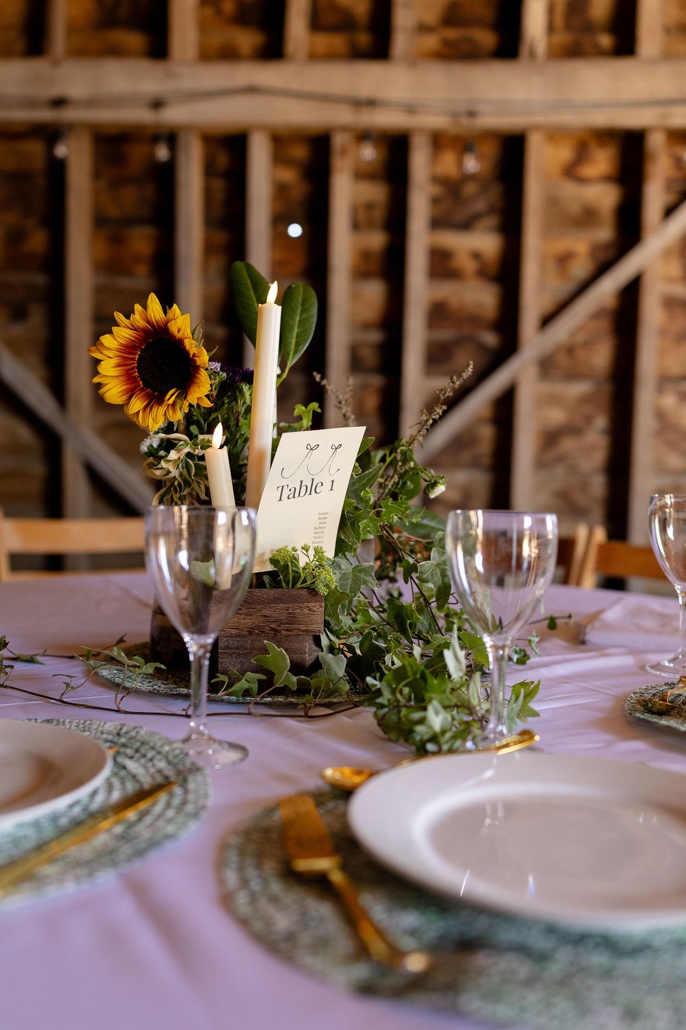 Elegant wedding reception table settings with white candles, sunflowers, and greenery decorations on a white tablecloth.