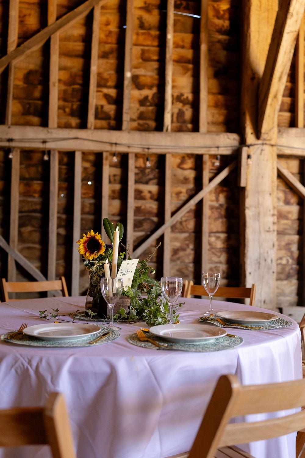 Elegant table settings with white linens and floral centerpieces in a rustic barn venue.