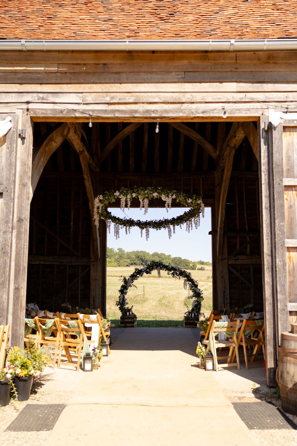 Rustic barn wedding venue with wooden beams and floral arch overlooking countryside.