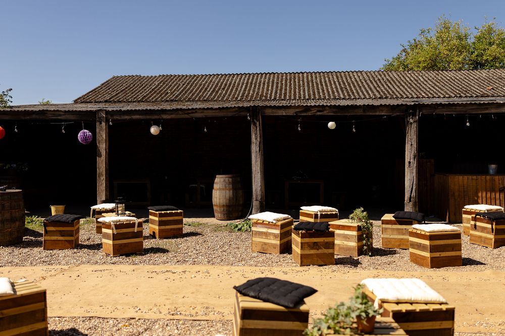 An outdoor wedding venue with wooden benches and wine barrels under a covered patio.