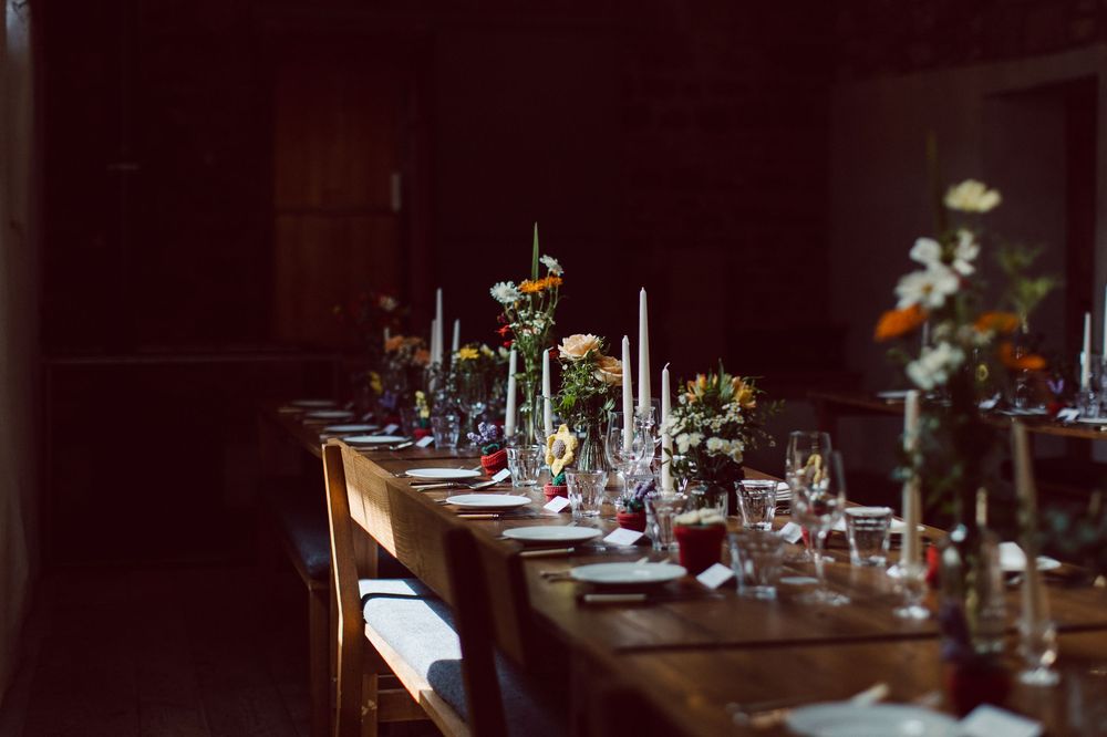 Elegant place settings with wine glasses and cutlery arranged on dark wooden tables in a dimly lit restaurant interior.