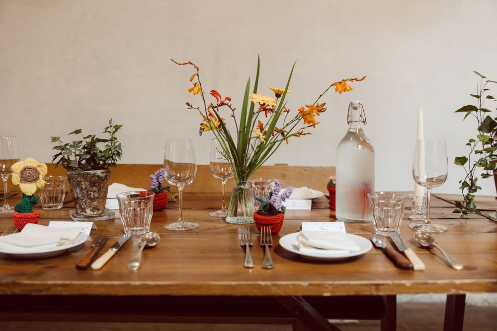 Rustic wooden table set with white plates, wine glasses, and small floral centerpieces in a restaurant setting.