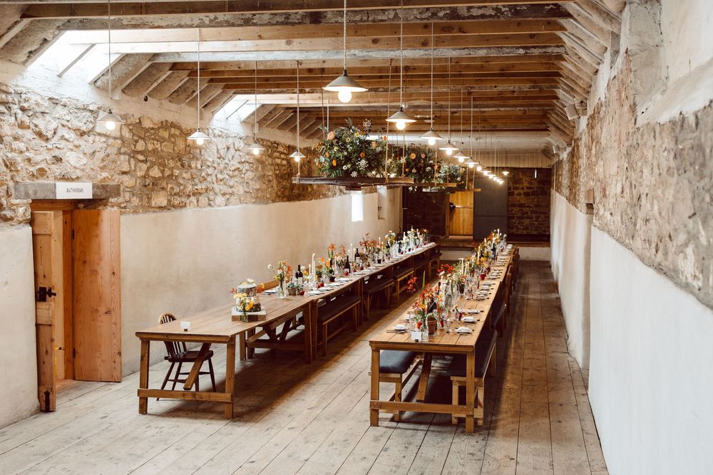 Long wooden banquet tables arranged in rows inside a historic stone barn with vaulted ceilings.
