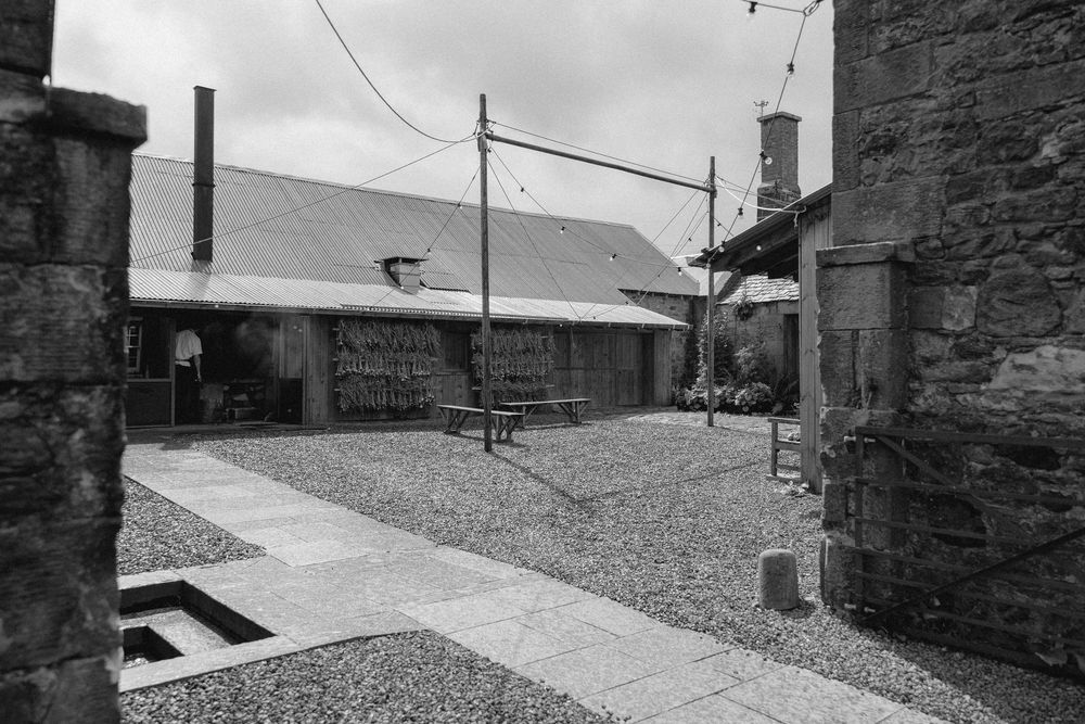 Black and white panoramic view of a rural stone building complex with gravel paths and stone walls.