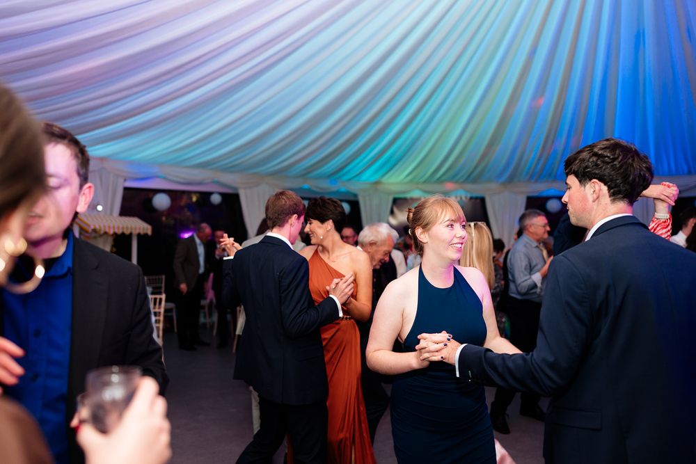 Wedding reception dance floor filled with guests under colorful blue and purple lighting creating a festive atmosphere.