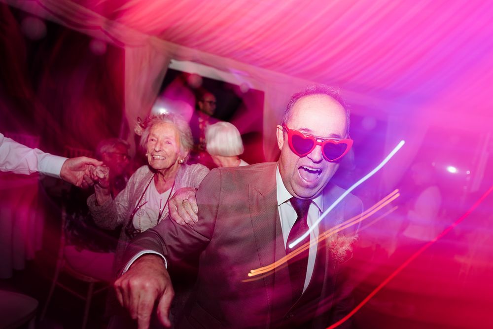 People dancing and celebrating at a party with vibrant pink and purple lighting creating an energetic nightclub atmosphere.
