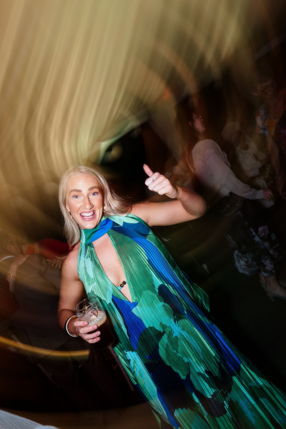 Person dancing energetically in a flowing blue and green dress at a nightclub with motion blur effects.