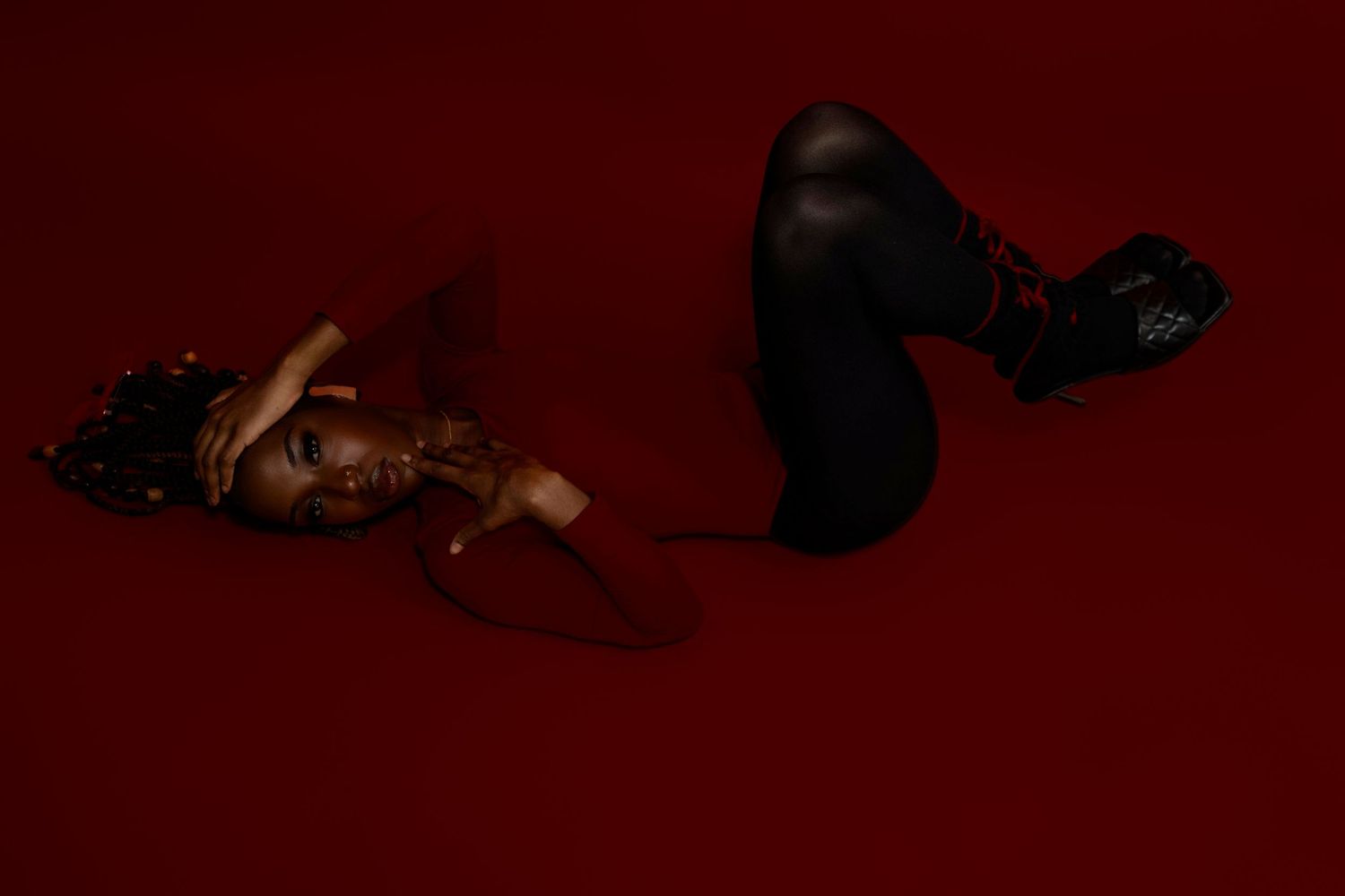 Woman lying on red floor in dark dramatic editorial fashion portrait with chunky boots.