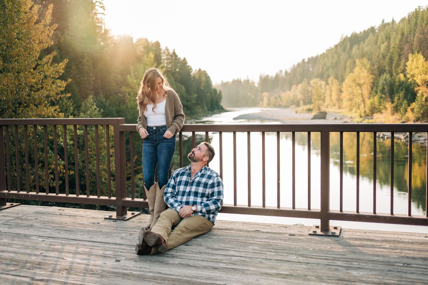 Two people enjoy a peaceful autumn evening on a wooden deck overlooking a serene lake surrounded by evergreen forest.