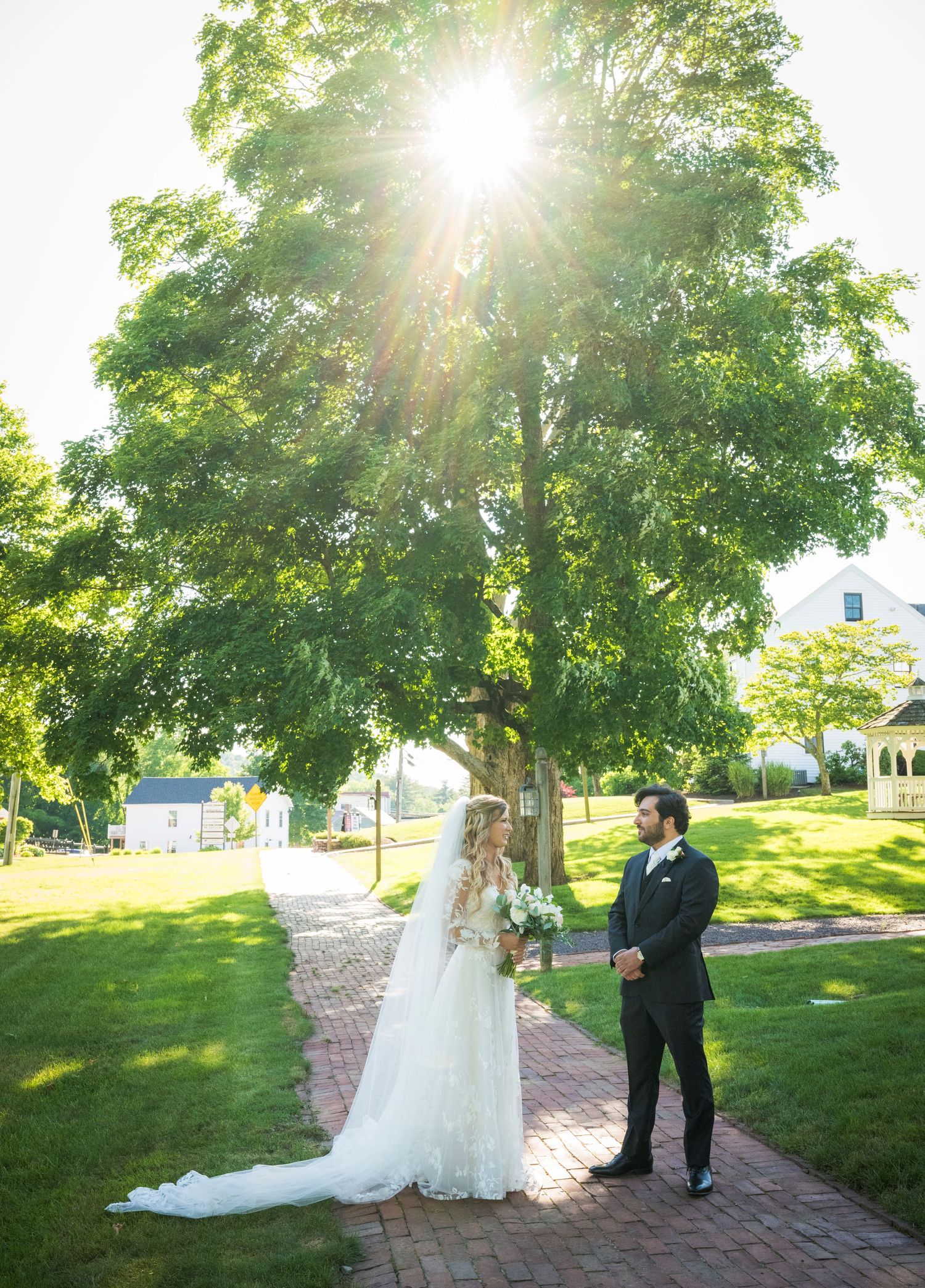 A couple poses for a wedding photo in front of a red brick building with a blooming tree in spring.