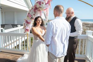 A wedding ceremony on a white deck with a pink floral arch and ocean backdrop.