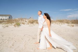 A couple strolls along a sandy beach with coastal homes visible on the dunes.