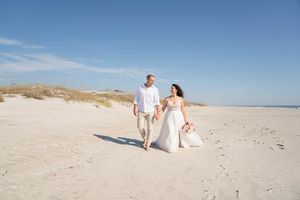 Wedding couple enjoys romantic moments on a sunny beach with coastal scenery.