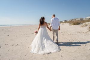 Newlyweds stroll together on a pristine beach with dunes in the background.