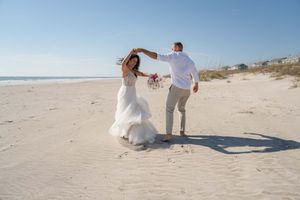 A couple in wedding attire shares playful moments on a sun-drenched beach.
