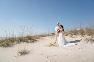 A wedding couple creates romantic photos among the sea oats on a pristine beach.