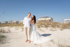 A romantic beach wedding photo shoot with a couple walking along white sand dunes.