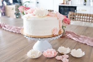 Elegant white wedding cake decorated with pink roses and petals on a white cake stand.