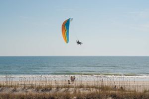 Beach scene with colorful parasailing activities over ocean waves.