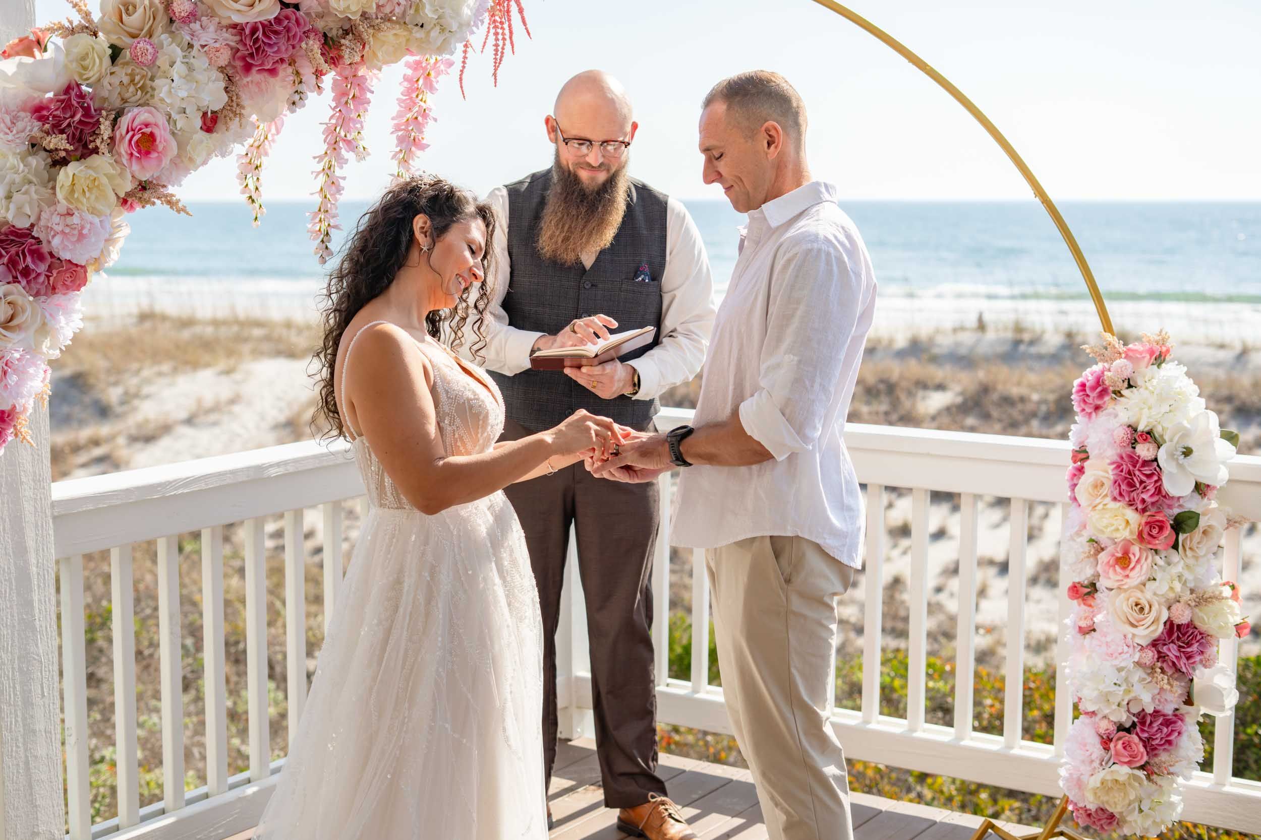A ceremony moment under a floral arch with the ocean as backdrop.