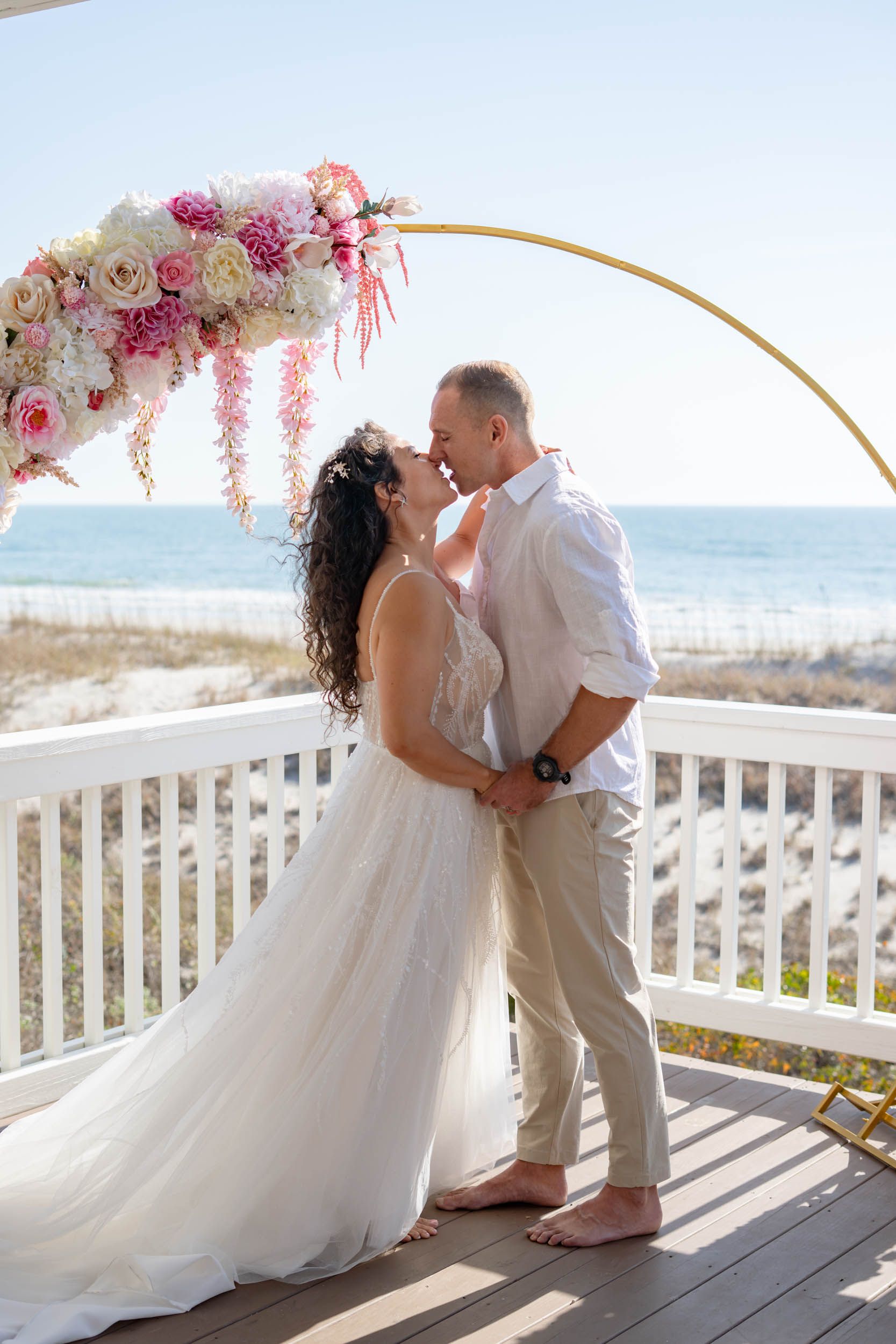 A romantic moment under a pink and white floral arch overlooking the ocean.