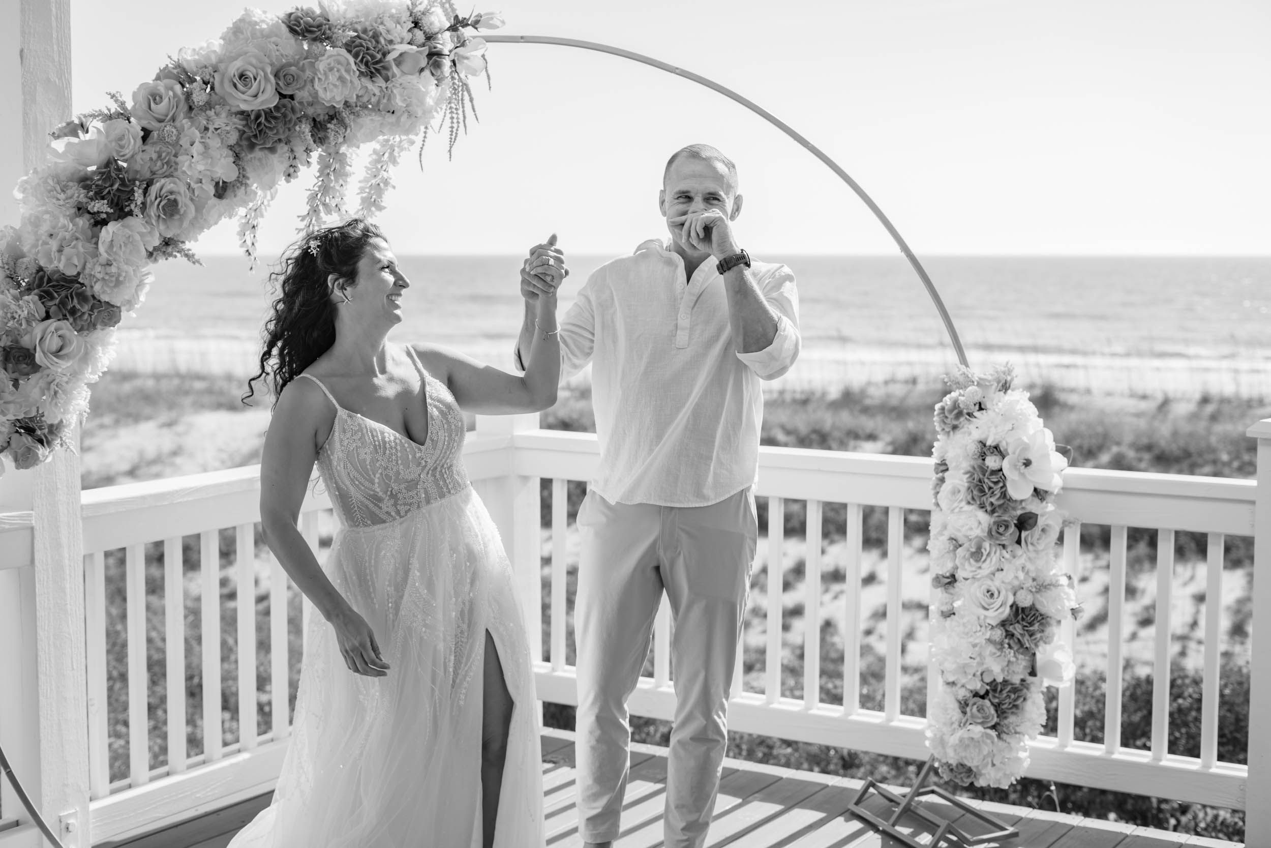A joyful moment captured under a floral arch on an oceanfront deck.