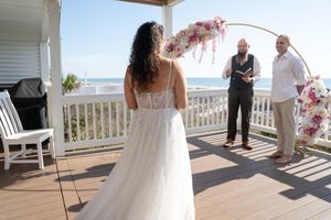Wedding guests gather on a sunny deck overlooking the ocean during an intimate ceremony.