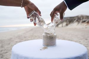 Hands pouring sand into a ceremonial vessel during a beach wedding ritual.