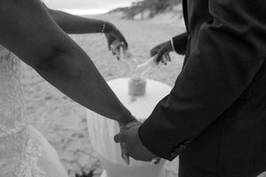 Black and white photo of newlyweds holding hands during their beach ceremony.