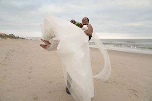 Wedding couple runs playfully along the shoreline with dress flowing in the wind.