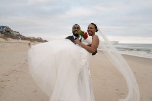 Bride's white dress flows in the ocean breeze during beach wedding photos.