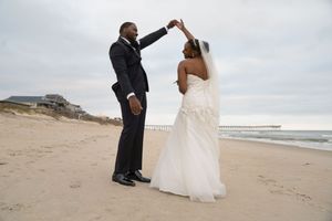 Wedding couple poses playfully on a cloudy beach with waves in the background.